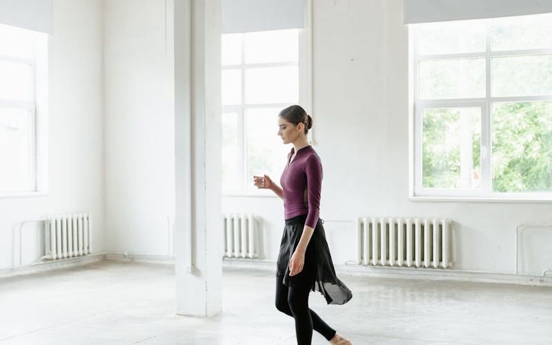 Woman performing a fluid motion exercise in a spacious, light-filled studio.